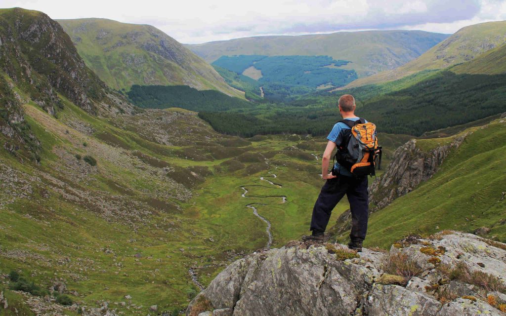 A walker standing on a rock enjoying the view over Corrie Fee in Glen Clova, Scotland