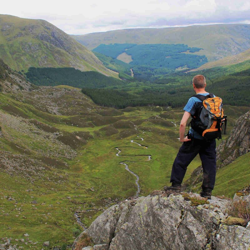 A walker standing on a rock enjoying the view over Corrie Fee in Glen Clova, Scotland