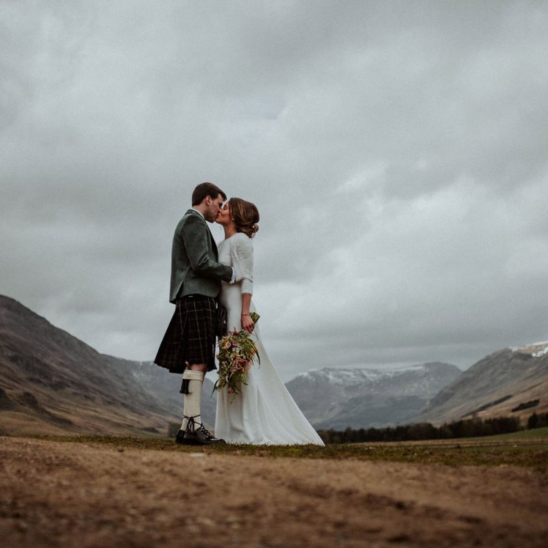 A bride and groom embracing in Glen Clova with snow capped mountains by them. Photography by Burfly. https://burfly.co.uk/