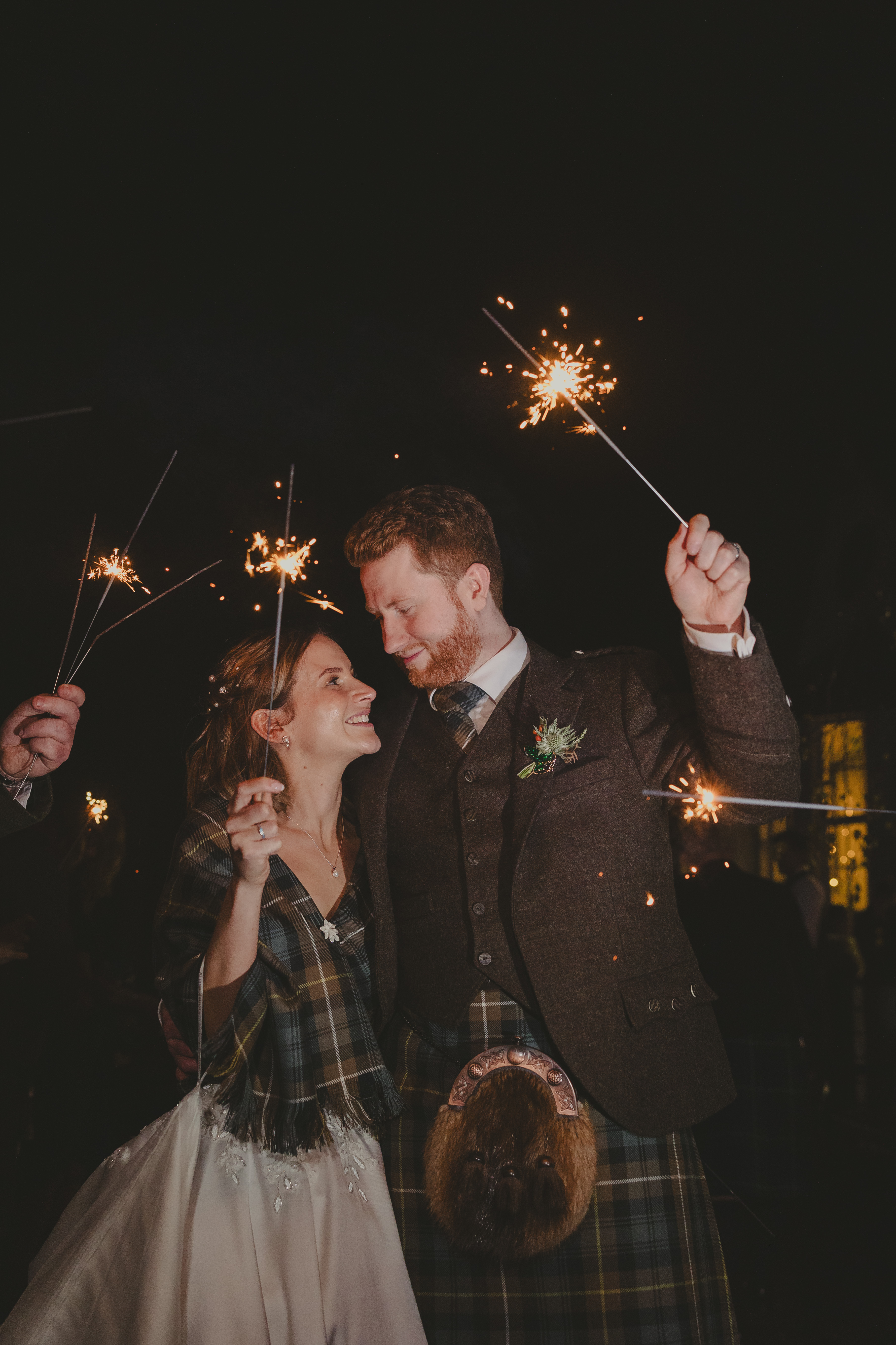 Bride and Groom after their wedding reception outside of Glen Clova Hotel holding sparklers with their guests Photography By Rhea https://byrhea.co.uk