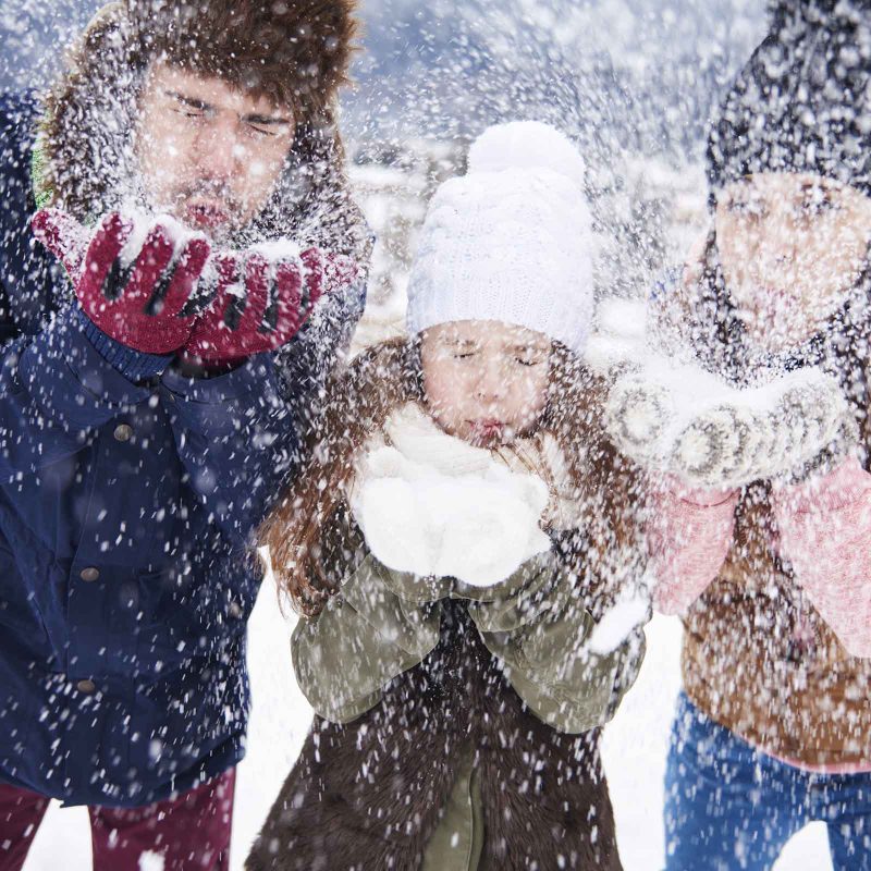 A family blowing snow out of their hands