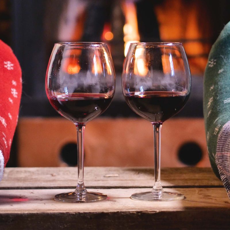 Two glassed on wine by the fireplace and two pairs of feet being warmed by the fire