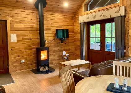 A cosy woodopen plan living area with a lit woodburner in a Hideaway Lodge at Glen Clova Hotel and Lodges in Scotland