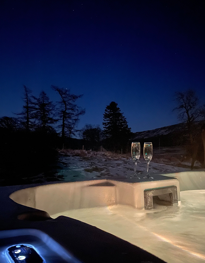 A hot tub at night with two champagne glasses on it at a Clova Lodge at Glen Clova Hotel