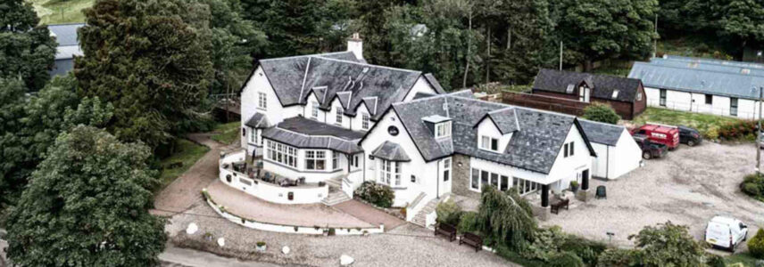 The exterior of Glen Clova Hotel with rolling Scottish hills in the background