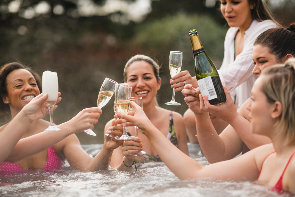 Small group of female friends socialising and relaxing in the hot tub on a weekend away. They are celebrating with a glass of champagne.